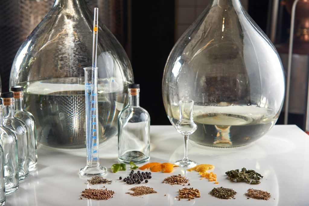 vários frascos usados para destilação do gin em meio aos ingredientes base para a bebida
