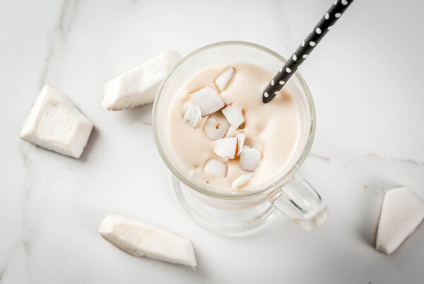  Batido de coco com leite - com café, creme de coco (leite), pedaços de coco. Em uma mesa de cozinha de mármore branco.