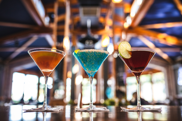 Três coquetéis coloridos em taças de vinho no balcão de um bar ou restaurante