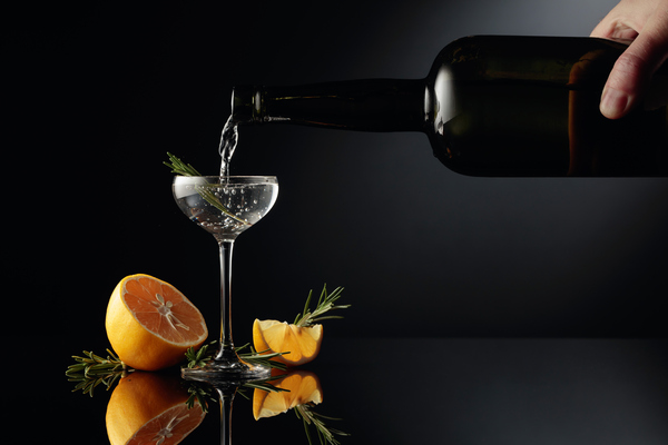 O gin é servido em um pequeno copo de uma antiga garrafa de vidro escuro. Uma bebida alcoólica forte com limão e alecrim em um fundo preto reflexivo.