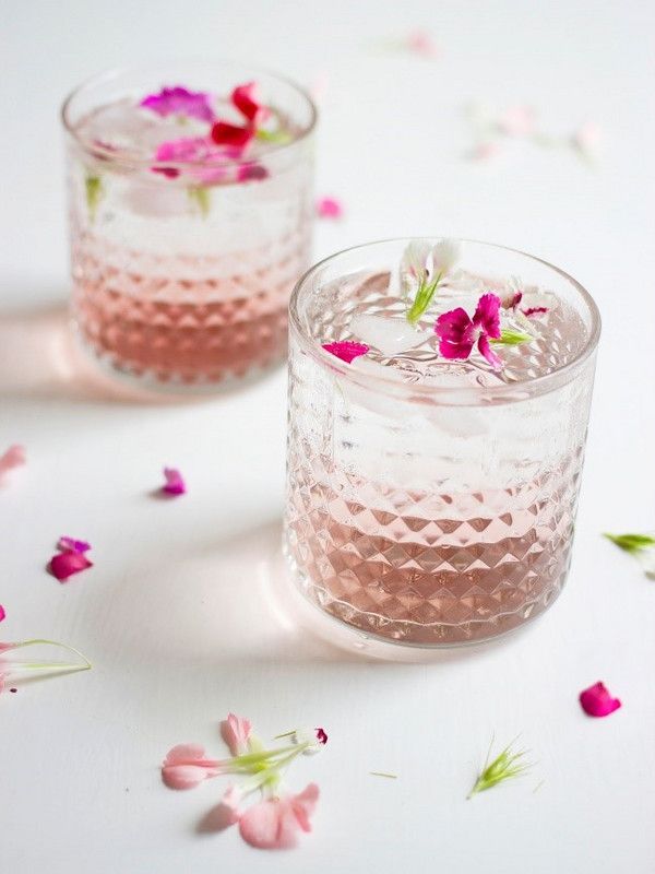 dois copos de um drink rosado com pequenas flores na decoração
