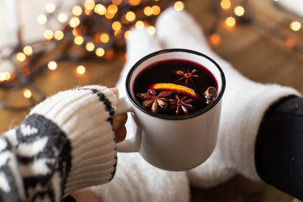 Composição com uma caneca de vinho tinto quente com especiarias. Atmosfera aconchegante de férias, meias de pelúcia, agasalho quente, luzes de Natal em um fundo escuro.