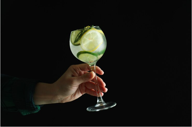 Gin-para-empresas: mão feminina segurando uma taça de vidro, dentro da taça existe gelo, rodelas de limão e pepino