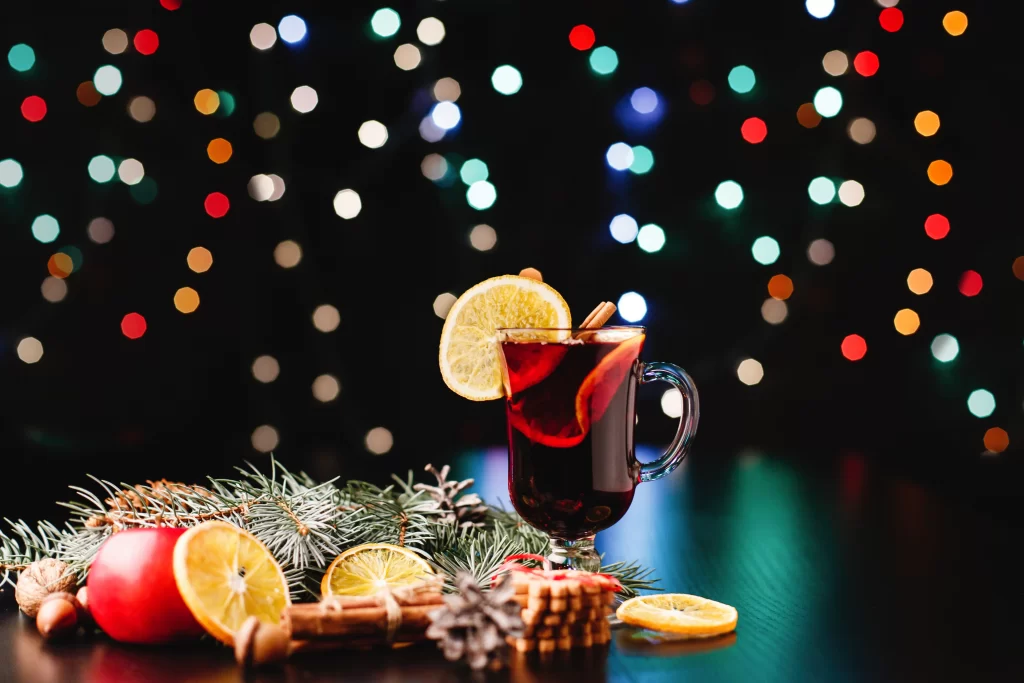 drinks natalinos com frutas e especiarias sobre a mesa, com luzes de Natal ao fundo 